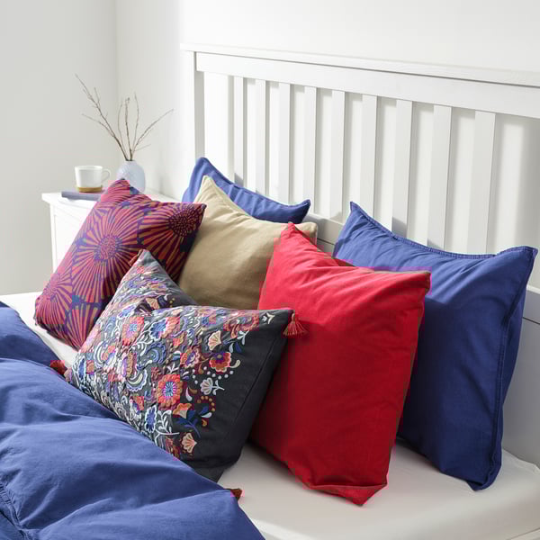 Bed with colourful pillows. Red, blue, and patterned cushions on white bedspread.