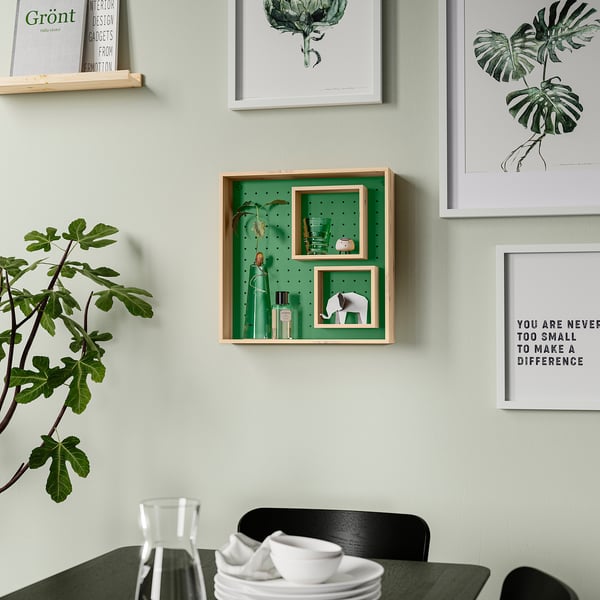 Green wall shelf with adjustable inner shelves, decorated with items and plants, surrounded by art and a black chair with crockery.
