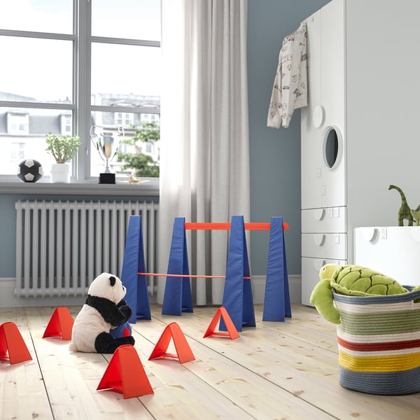 Blue & orange kids obstacle course with cones and panda. Near white furniture, large window.