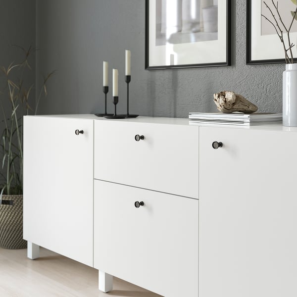 White cabinet with black knobs, featuring anthracite finish and rounded details. Top holds candlesticks and decor items.