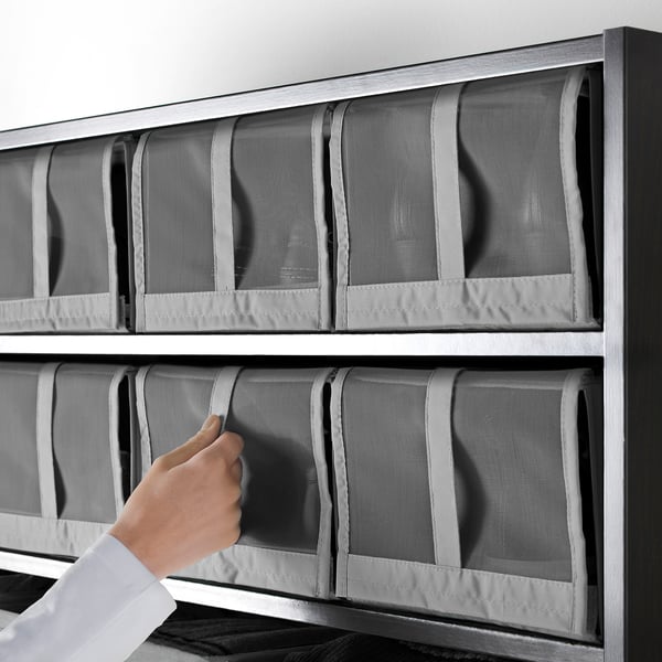 Person placing mesh SKUBB shoe boxes onto shelf. The boxes are organised and air circulates through mesh.