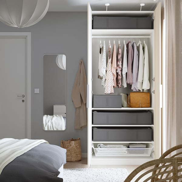 Bedroom with white SKUBB storage cases in an open wardrobe, holding folded clothes and a bag. A mirror and wicker basket are beside the wardrobe.