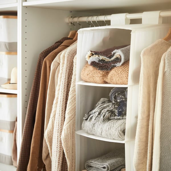 Well-organized closet with beige clothes; a hanging storage unit labelled SKUBB in white holds folded sweaters.
