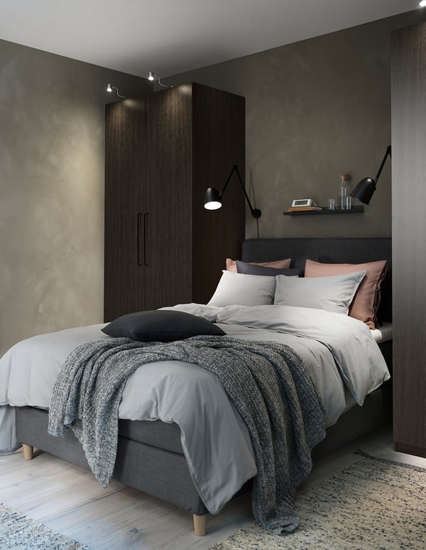 Modern bedroom with grey bedding, black SKURUP lamps on either side, grey rug, wood floor, and built-in dark wooden wardrobe.