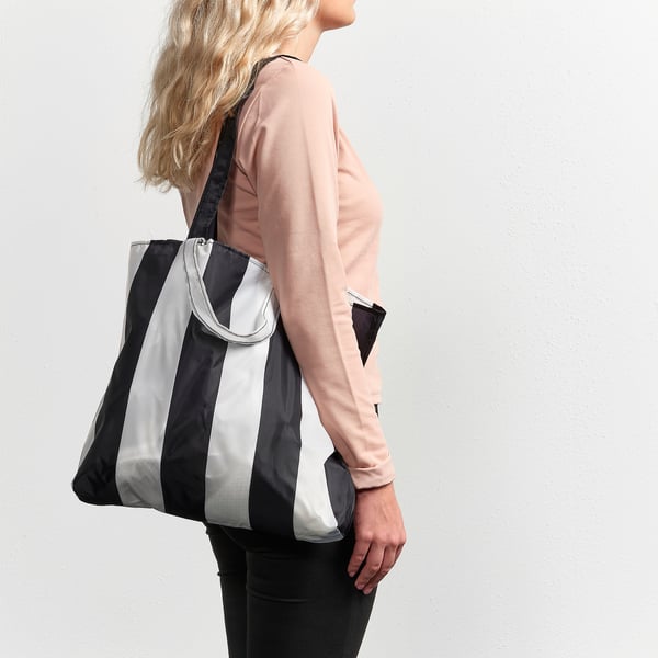Person holding black and silver bag, likely the SKYNKE, designed to be lightweight and versatile for shopping or travel.