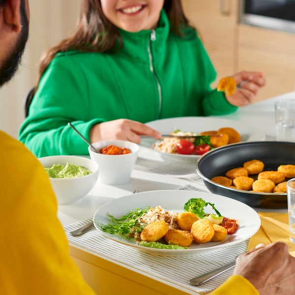 People eating SLAGVERK breaded wheat-based pieces with various side dishes on plates at a dining table.