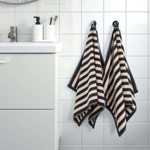 Black and tan striped SLÅNHÖSTMAL towels hang on hooks by sink with soap and toothbrushes.