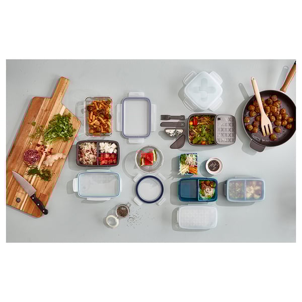 Top view of wooden cutting board, various food items, and colourful plastic containers of different sizes.