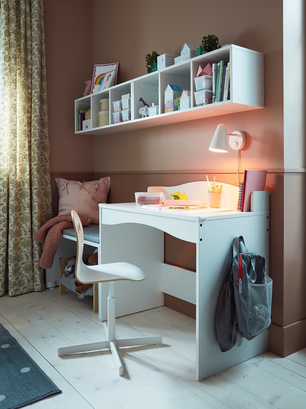 Small kids white study desk with adjustable chair, wall shelves with toys and books, under-bed storage, and bold lighting.