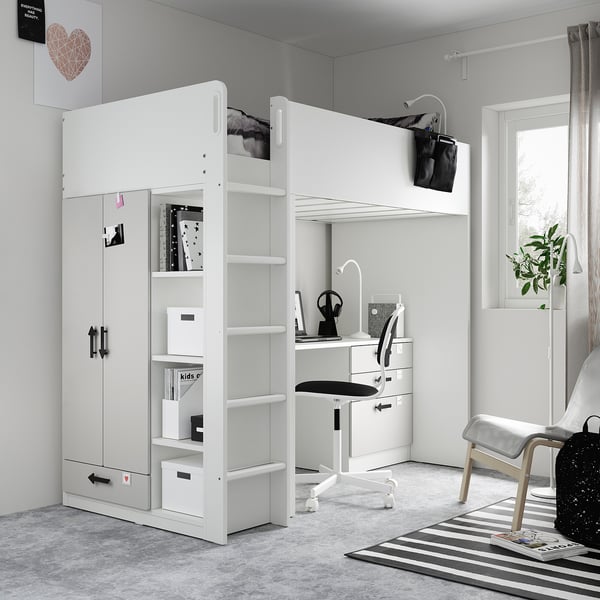 Modern white kids room with loft bed, desk, shelves, and wardrobe. Grey carpet, black chair, striped rug.