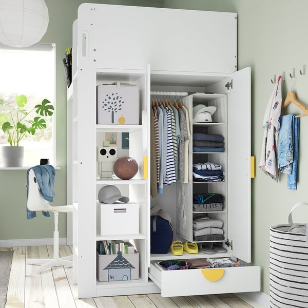 White SMÅSTAD kids loft bed with desk, wardrobe, and bookcase. Wardrobe open, displaying neatly organised clothes and storage.