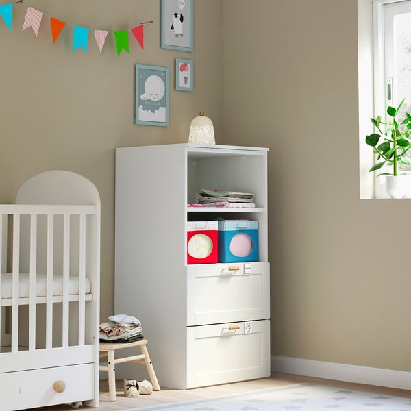 Small white nursery with baby crib, low stool, and storage unit. Colourful decor and books.
