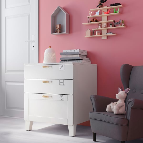 Small childrens room with pink walls, white SMÅSTAD chest of drawers, grey chair, stuffed unicorn, books, and toys on shelves.