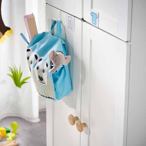 A kids blue backpack with giraffe design hangs on a white wardrobe with wooden hooks.