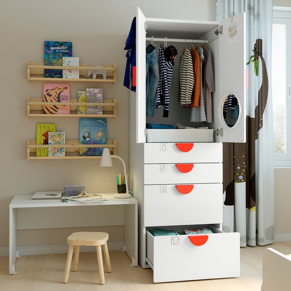 Childrens room with white SMÅSTAD wardrobe, wooden shelves of colourful books, a small desk with lamp, and a round stool.