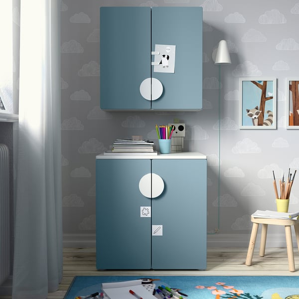 Blue SMÅSTAD kids storage unit with soft-close hinges and round handles against cloud-patterned wall, storing crafts and books.