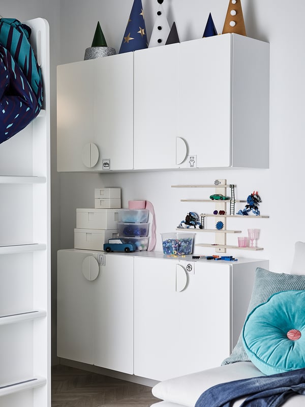 Modern white childrens storage unit with cabinets and shelves, holding toys and books, adorned with colourful decorations.