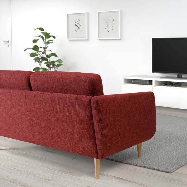 Cosy red retro sofa with wooden legs and soft cushions, paired with a tv on a white stand.