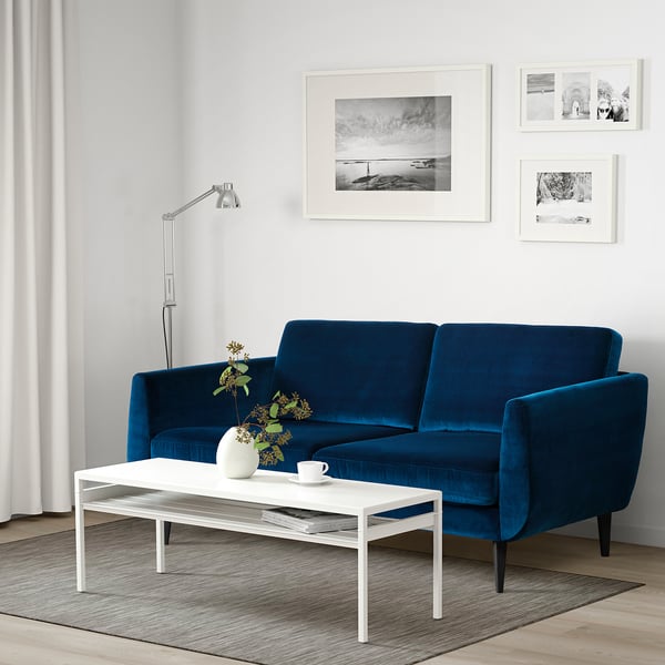 Modern living room with SMEDSTORP blue velvet sofa, white coffee table, minimalist design, art prints, floor lamp, and vase.