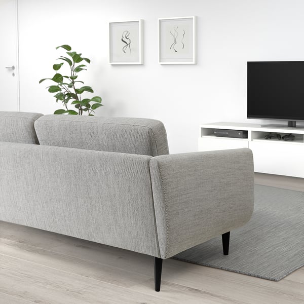 Grey fabric sofa with cone legs beside a tv on stand, plant on back, white wall art.