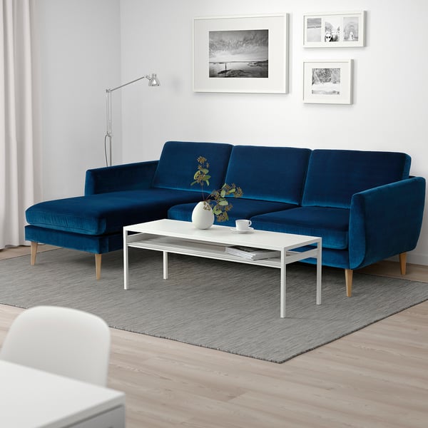 Blue velvet sectional sofa with wooden legs, photos, coffee table, vase, teaset, magazines.