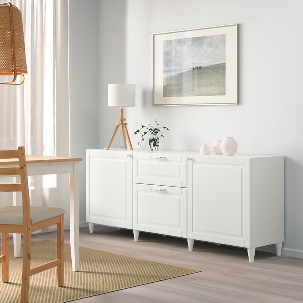 White SMEVIKEN sideboard with drawers, lamp, plant, vases, under coastal art.