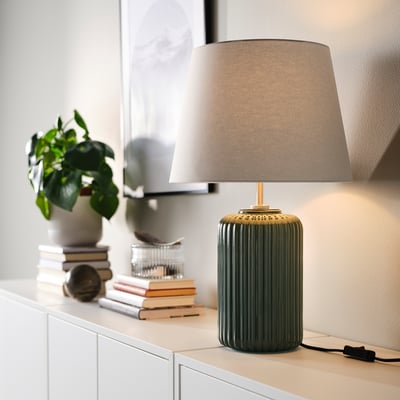 SNÖBYAR green lamp with gold accents. Textured shade, ceramic base. Small plant, books beside.