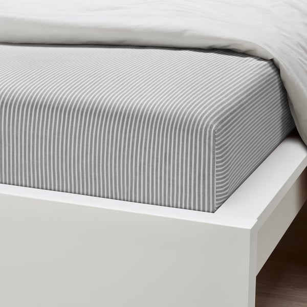 Crisp white bed with grey striped fitted sheet, neatly tucked, showing quality cotton texture.