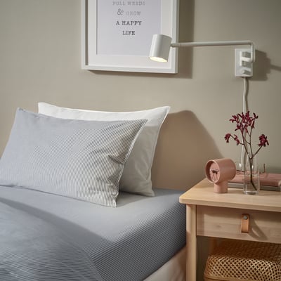 Bedroom with striped pillow, lamp, flowers, and wall quote.