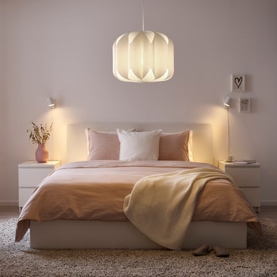 Cosy bedroom: central bed, warm lights, pink pillows, decor on nightstands, soft walls, rug, slippers, pendant light.