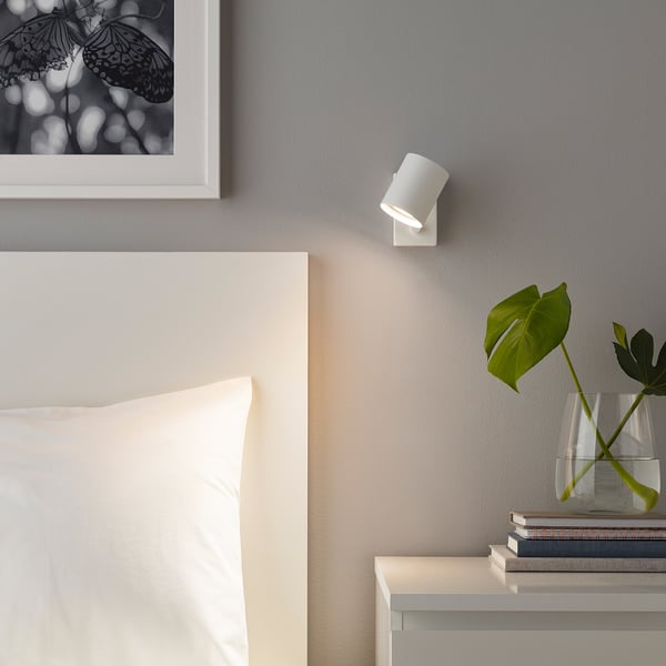 Modern bedroom with SOLHETTA led wall light, bedside table, pillow, plant, and butterfly art.
