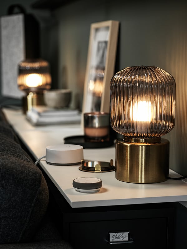 Modern bedroom with golden lamps on bedside tables, one lit, alongside tech devices and a black headboard.