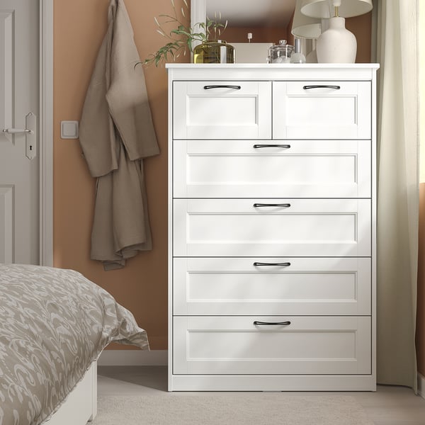 White SONGESAND 6-drawer chest with handles. Beside bed, topped with decor, taller than bed and plant.
