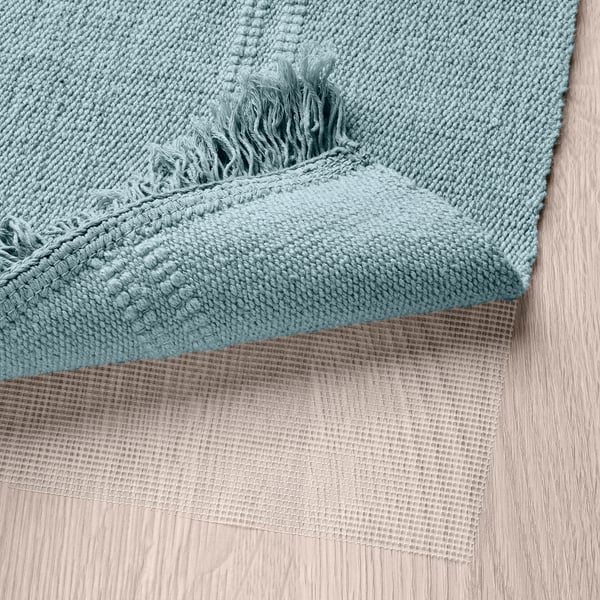 Green woven cotton rug, reversible, machine washable, laid on wood floor. Fringe detail visible.