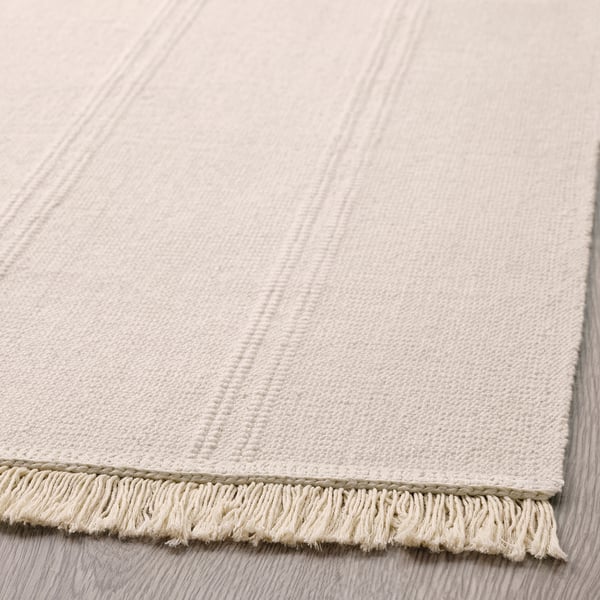 Light beige textured rug with fringe edges on a wooden floor.