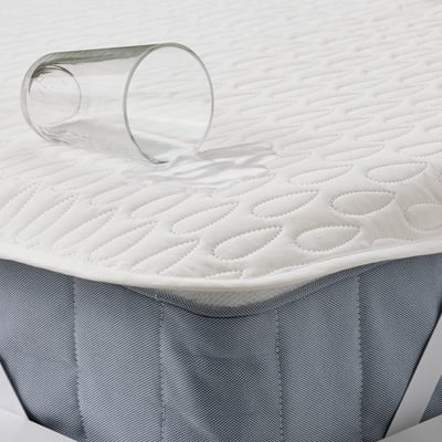 A rolled-up white waterproof mattress protector with a glass of water on top, demonstrating its spill-proof feature.