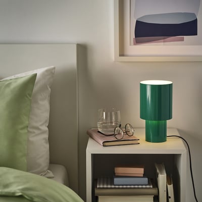 Modern bedroom with green SPETSBOJ lamp on white bedside table, books, and files.