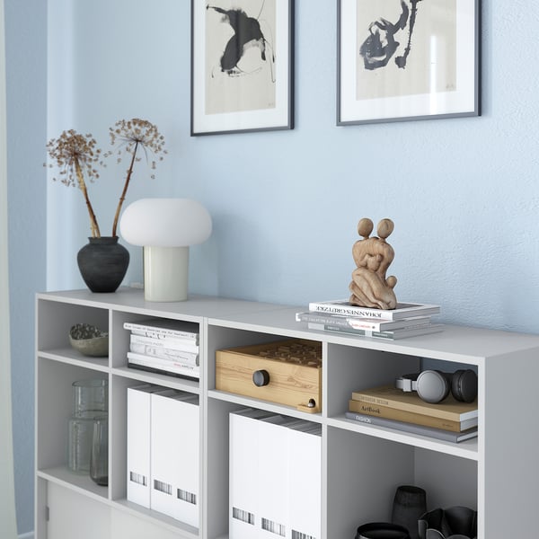 White shelf unit with drawers, books, decor, and lamp.
