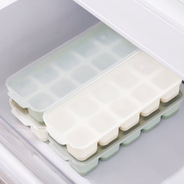 Ice cube trays with lids sit inside a freezer drawer. Trays have covers for easy handling and prevent spills.
