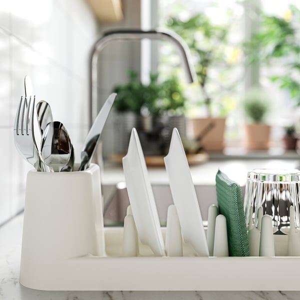 White kitchen dish drainer holding cutlery, plates, glasses, and mugs. Efficiently organises and dries dishes in limited space.
