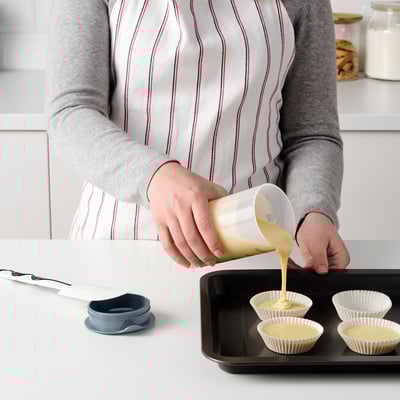 Person pouring liquid from a graduated shaker into muffin cups.