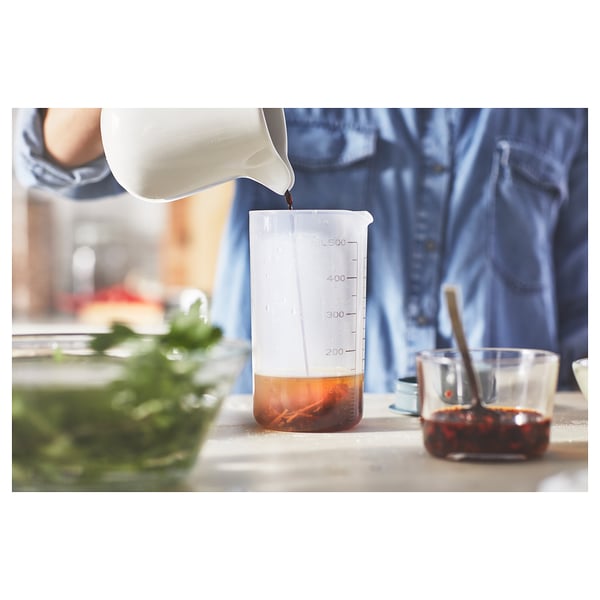 Person pours liquid into a clear, white, and brown graduated measuring cup, surrounded by other kitchen items.