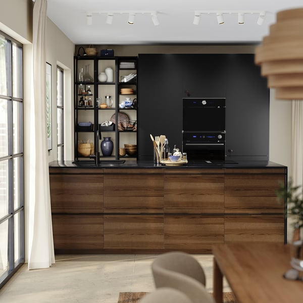 Modern kitchen with dark brown stained ash wood cabinets and black built-in appliances. Shelves display various decorative items.