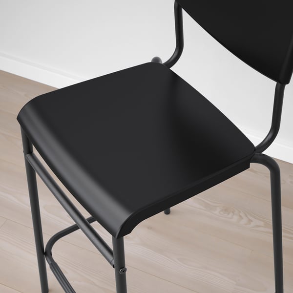 Black bar stool with sleek, curved metal frame and padded seat on light wooden floor.