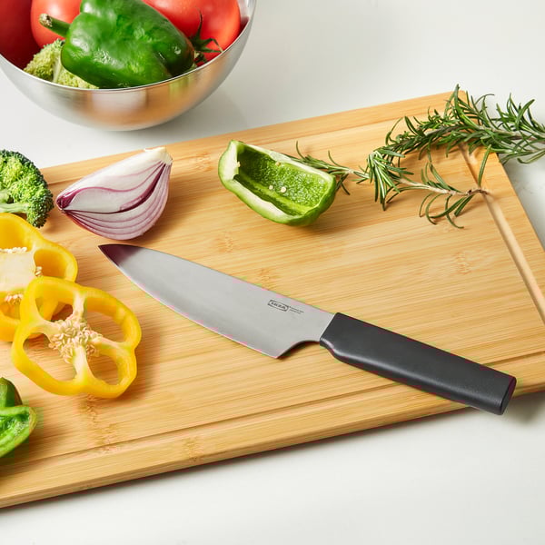 Wooden cutting board with knife, sliced vegetables: pepper, onion, garlic. Bowl with more veggies, rosemary sprig.