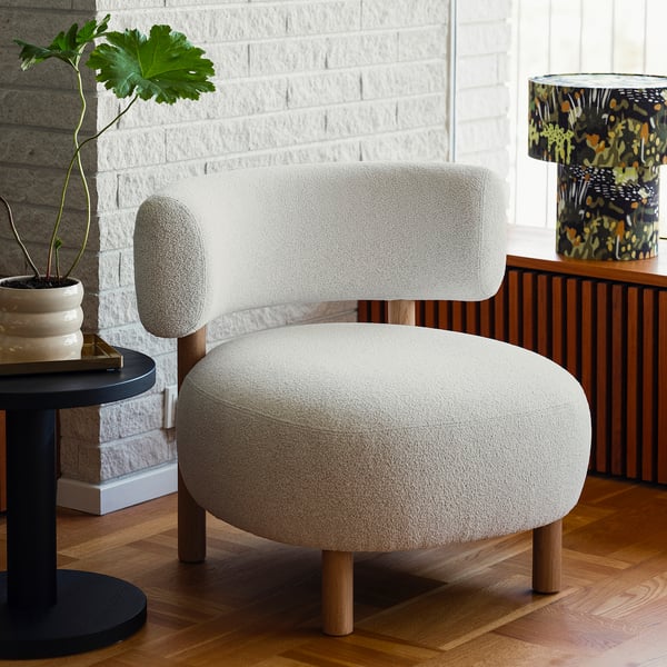 Modern scandinavian armchair, light grey, round & curved, oak legs, cozy, near plant & lamp.