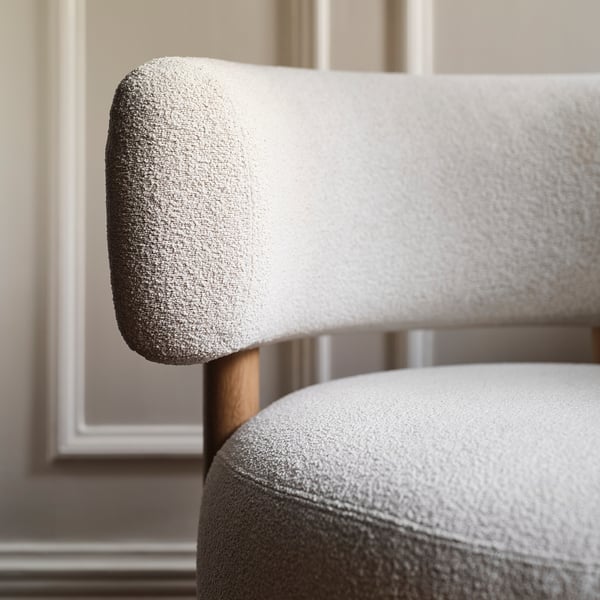 Close-up of a modern, high-quality chair. Soft, textured fabric covers plush back and seat, atop solid wooden legs.