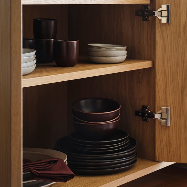 Wooden cabinet with rustic brown dishes; stacked dark brown bowls on middle & lower shelves, smaller bowls & cups on top shelf.