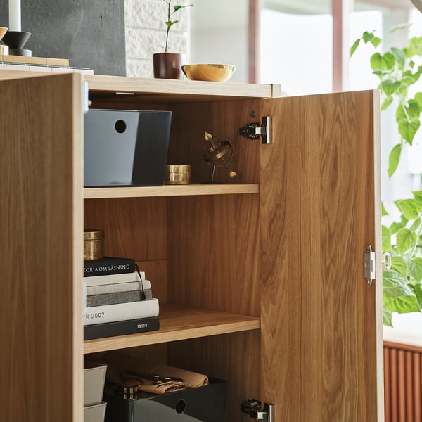 Wooden cabinet with soft-closing doors; one shelf holds books, another has small decorative items; adjustable interior shelves.