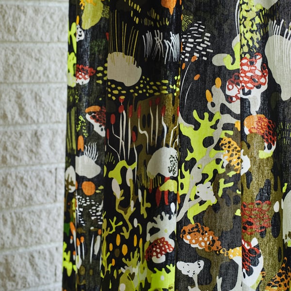 Patterned curtains with mushrooms & foliage on white brick wall.